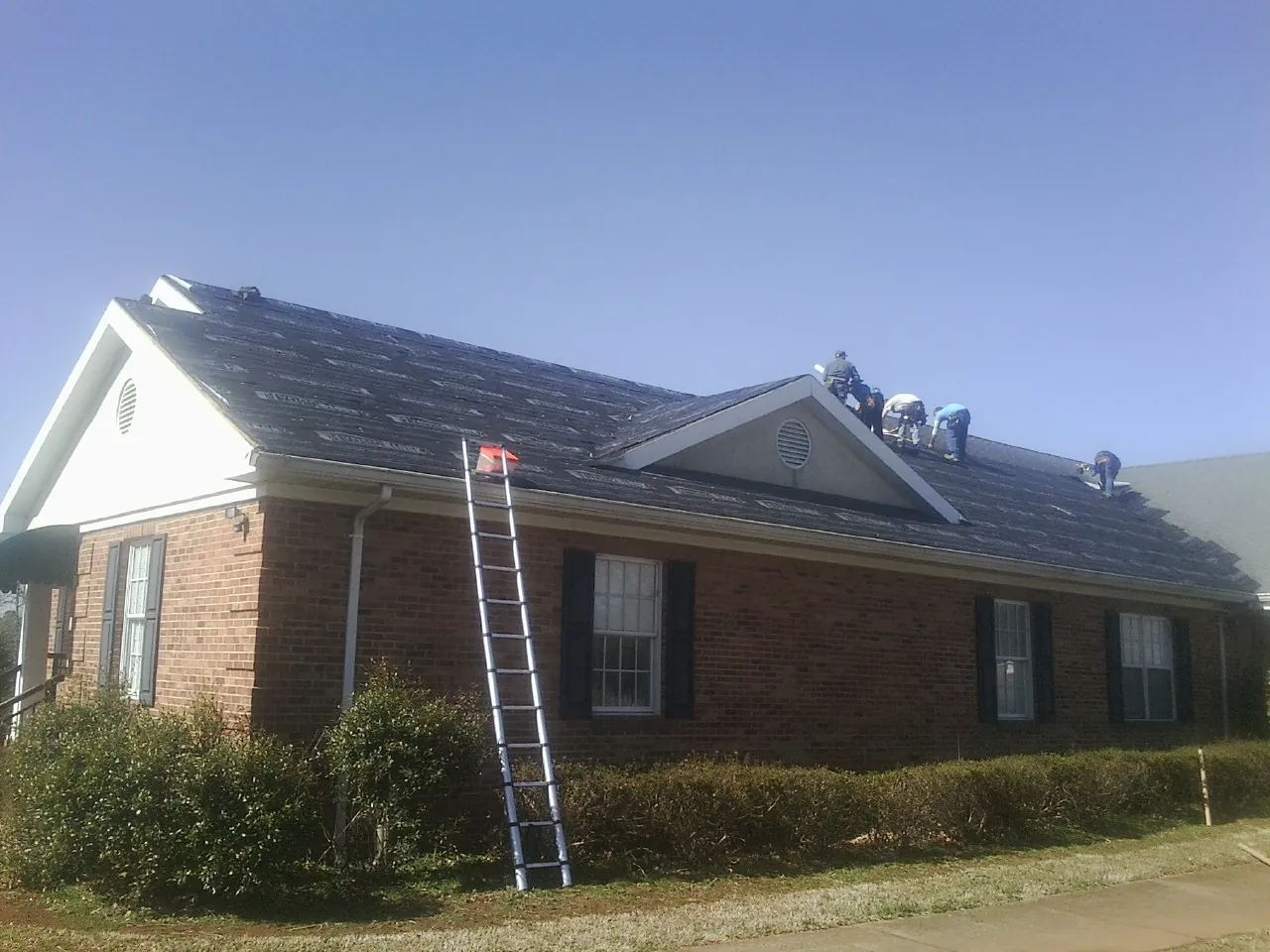 Crew tearing shingles off a brick ranch roof with a ladder set — Emergency Roof Repair work by our crew in Park Ridge