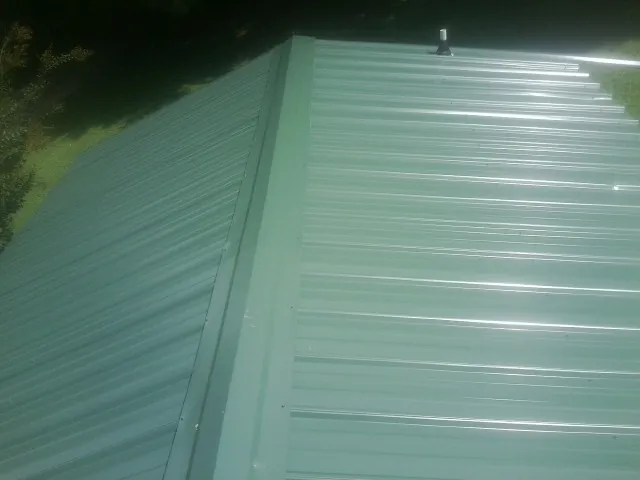 New green metal panels meeting at the ridge of a roof — Flat Roof Repair work by our crew in Park Ridge