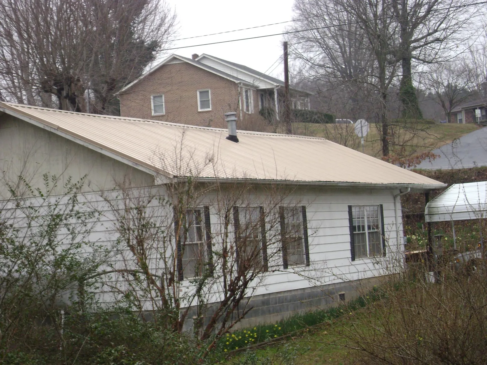 Tan metal roof on a white sided house set into a hillside — Commercial Roofing by Roofing Brothers in Park Ridge